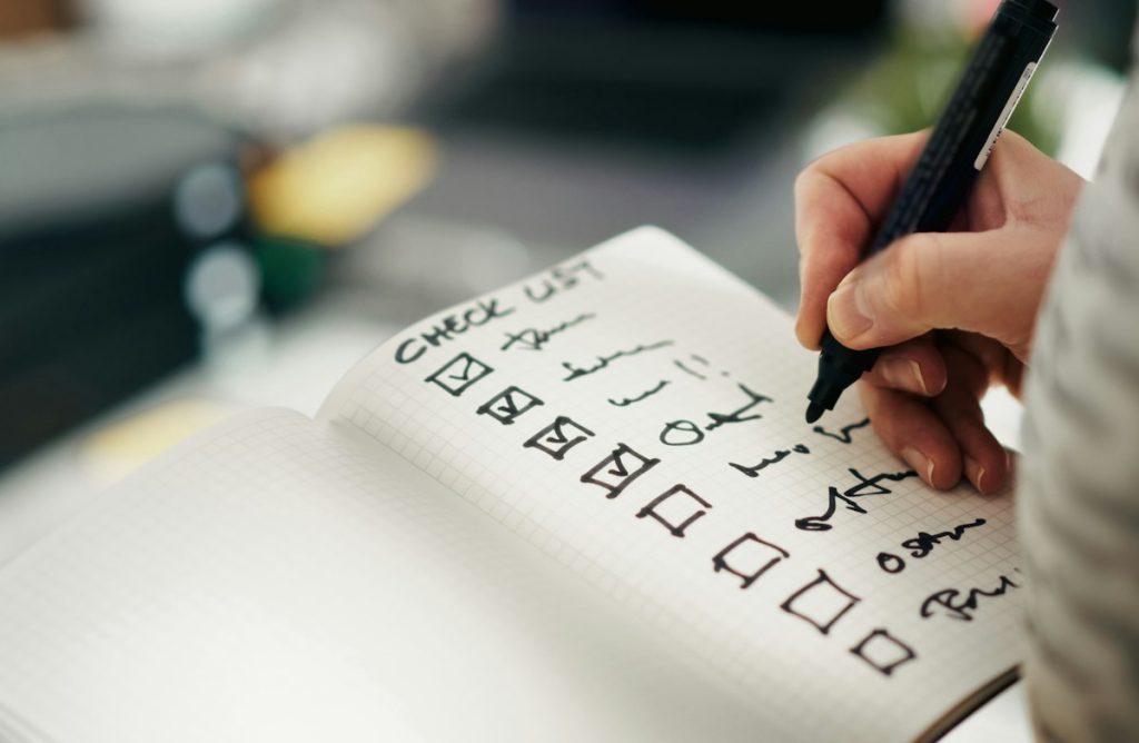 Hand holding a pen, checking off items on a printed checklist