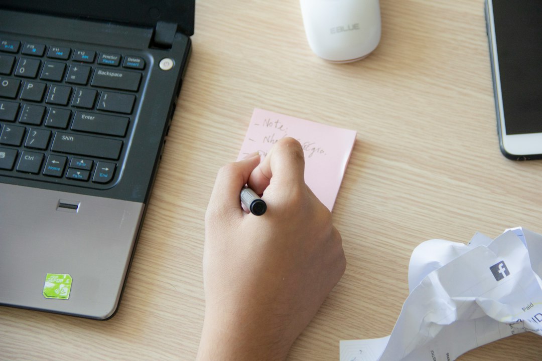Hand writing a personalised note on a sticky note next to a laptop