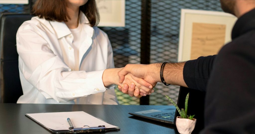 Two people shaking hands in front of a laptop