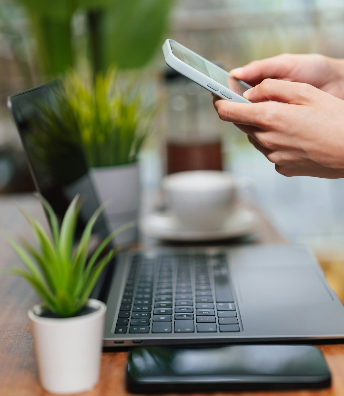Hand holding a phone next to an open laptop, representing a coordinated LinkedIn, email and phone outreach sequence