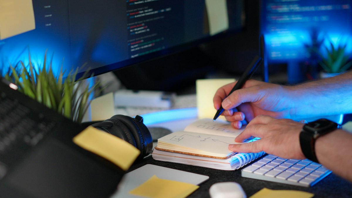 Hand marking checkboxes in a notebook next to a laptop while tracking a new SDR onboarding plan