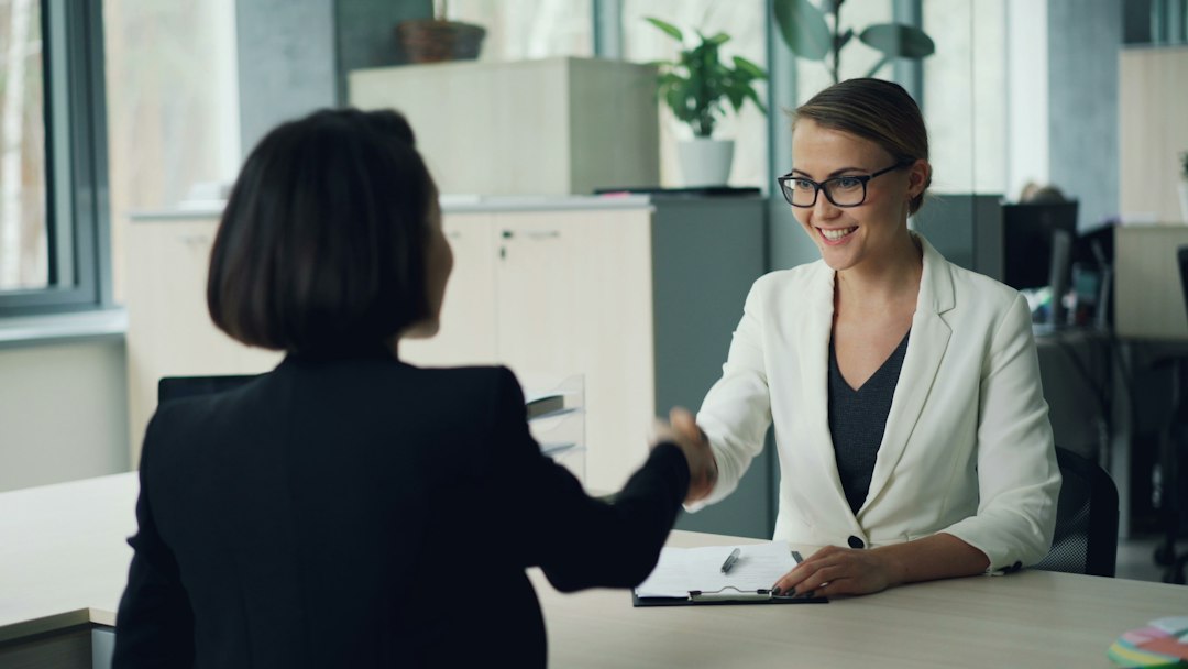 Two colleagues shaking hands across a desk during a sales handoff conversation