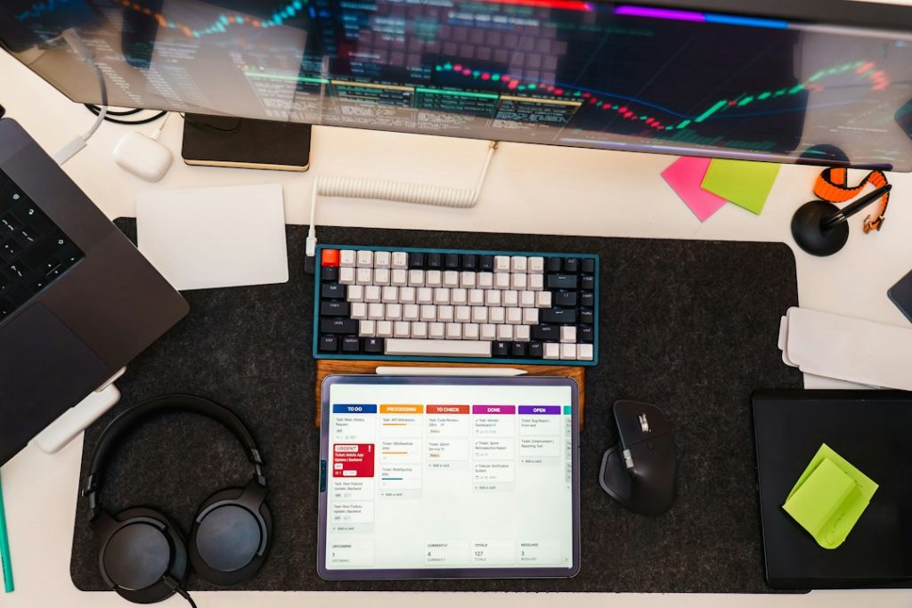 Desk workspace with a tablet showing a kanban task board next to a laptop and keyboard, representing a LinkedIn outreach tech stack