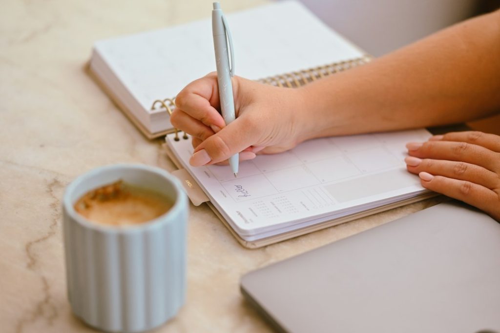 Hand writing in a desk planner next to a coffee cup, timing an outreach follow-up